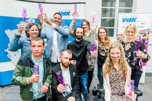 Eine Gruppe vilmA-Preisträger*innen hält jubelnd die Pokale in die Höhe.