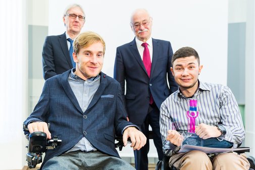 Zwei Männer im Rollstuhl, zwei stehend dahinter. Einer von den Rollstuhlfahrern hat einen vilmA-Pokal in der Hand.