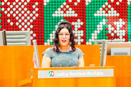 Eine Frau mit Brille und dunklen, hochgesteckten Locken steht am Rednerpult des NRW-Landtags und spricht.