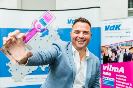 Ein vilmA-Gewinner streckt lächelnd den Preis Richtung Kamera.